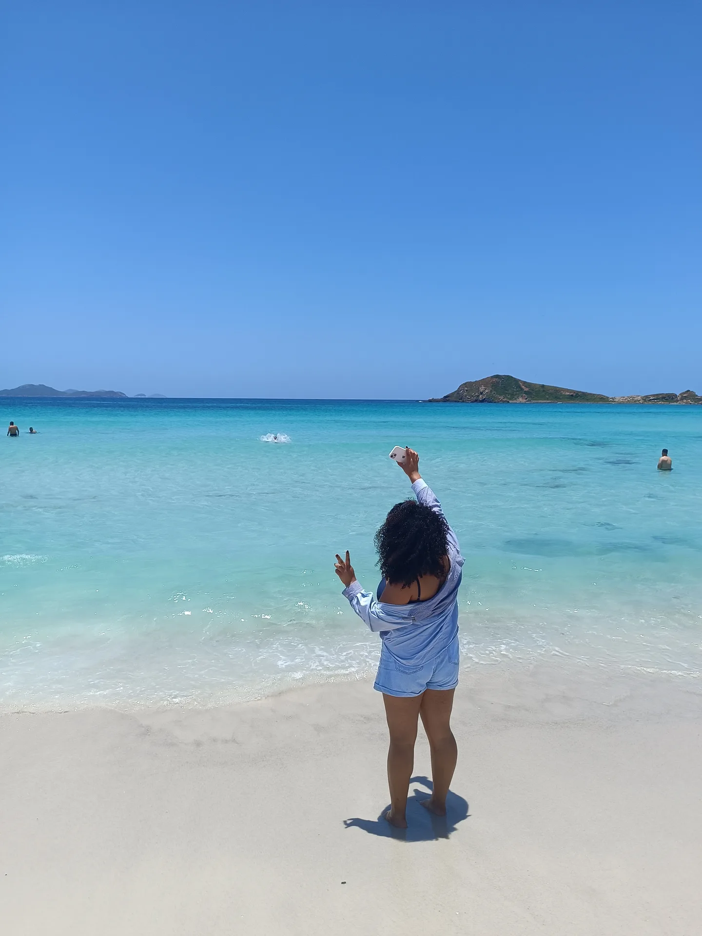 Mulher de costas na areia branca diante do mar turquesa de Arraial do Cabo